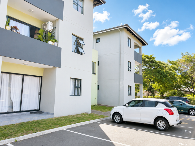 Exterior view of a modern apartment building featuring balconies, sliding glass doors, and dedicated ground-level parking spaces.