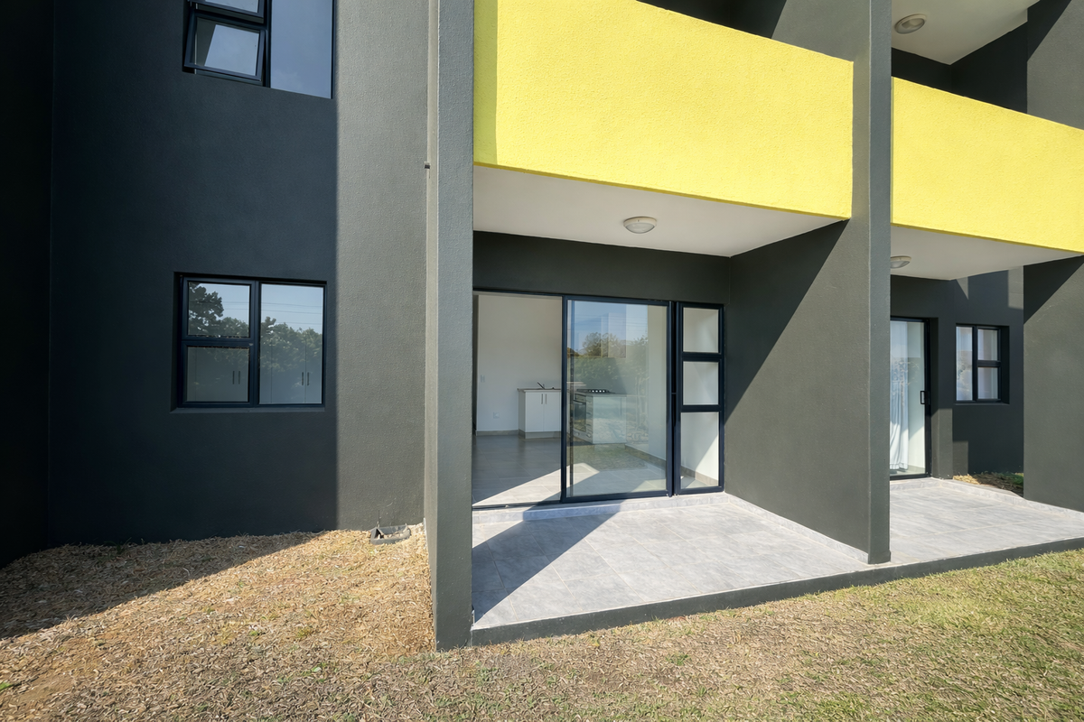 Modern ground floor apartment exterior featuring a tiled patio, sliding glass doors, and contemporary dark grey and yellow facade finishes.