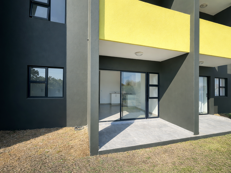 Modern ground floor apartment exterior featuring a tiled patio, sliding glass doors, and contemporary dark grey and yellow facade finishes.