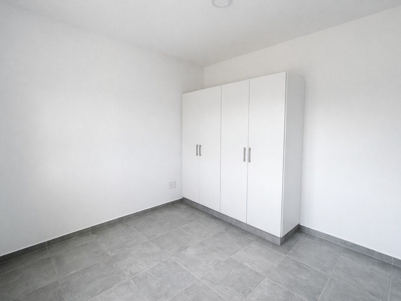 A clean, minimalist bedroom featuring neutral grey floor tiles and a modern white built-in wardrobe, offering a bright and versatile living space.