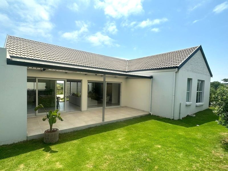 Rear view of the house featuring a covered patio with tiled flooring, sliding glass doors, and a well-maintained lawn.