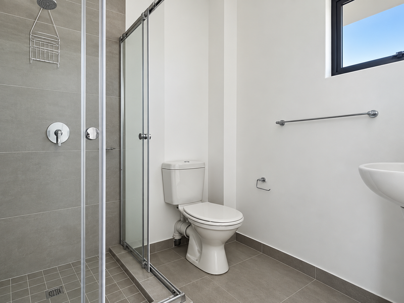 A modern, clean bathroom featuring a glass-enclosed shower, pedestal basin, and toilet with neutral grey floor and wall tiling.