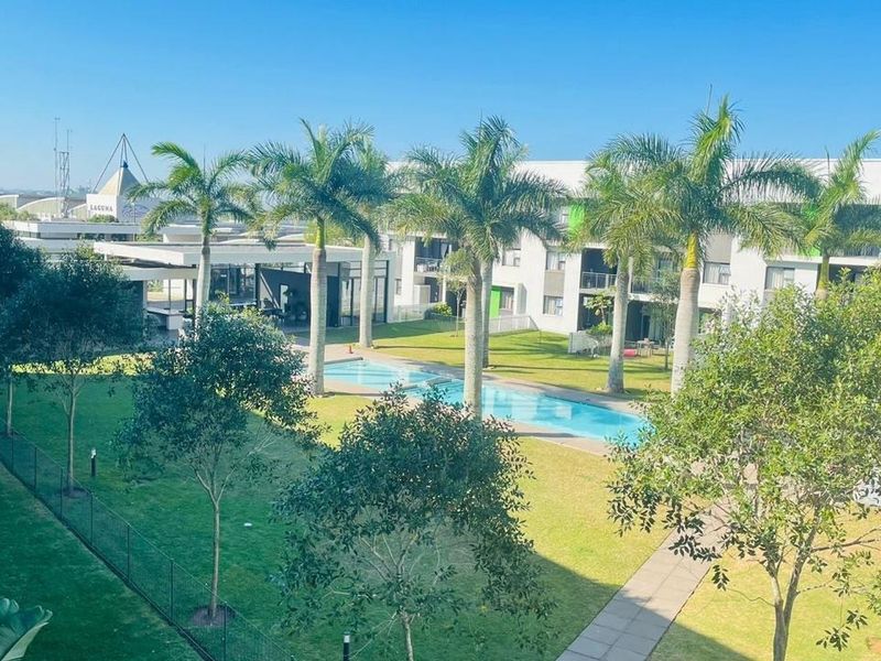 Elevated view of a well-maintained communal swimming pool area surrounded by landscaped gardens and palm trees within an apartment complex.