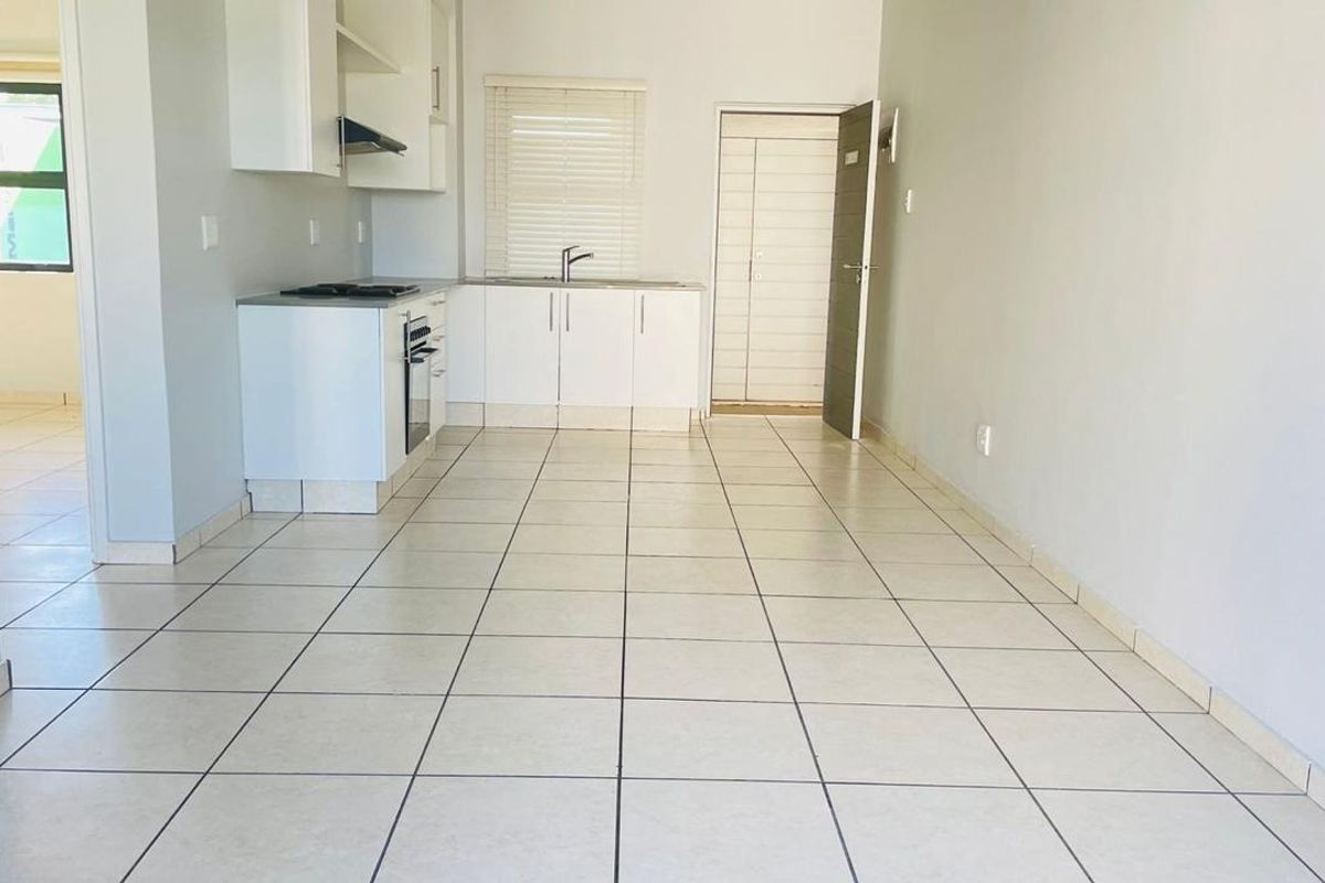 An open-plan kitchen and living area featuring tiled flooring, built-in cabinetry, and integrated cooking appliances, offering a clean and functional space.