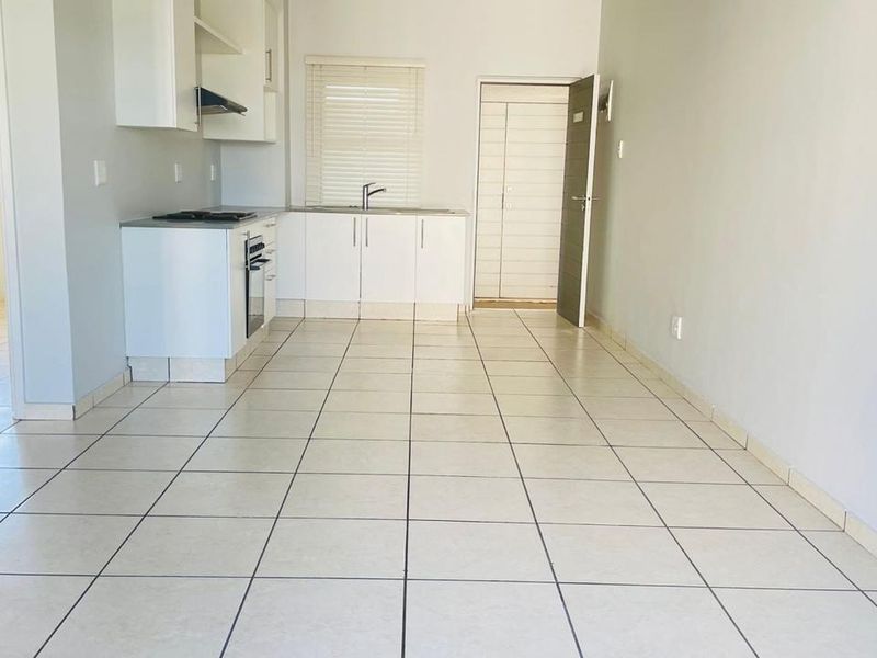 An open-plan kitchen and living area featuring tiled flooring, built-in cabinetry, and integrated cooking appliances, offering a clean and functional space.