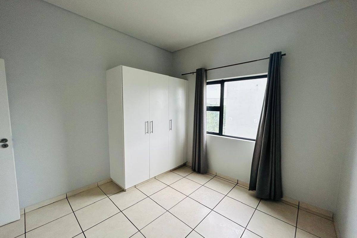 A clean, neutral bedroom featuring tiled flooring and a built-in white wardrobe, offering a bright and functional space ready for personalization.