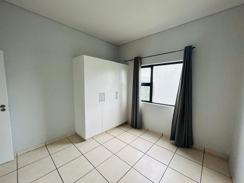 A clean, neutral bedroom featuring tiled flooring and a built-in white wardrobe, offering a bright and functional space ready for personalization.