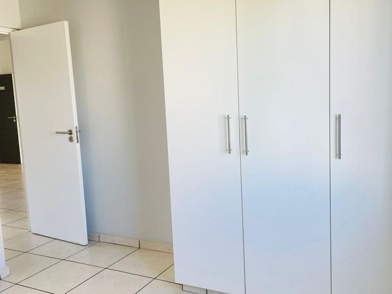 A clean, empty bedroom featuring neutral tiled flooring and white built-in cupboards, offering a blank canvas for personalization.