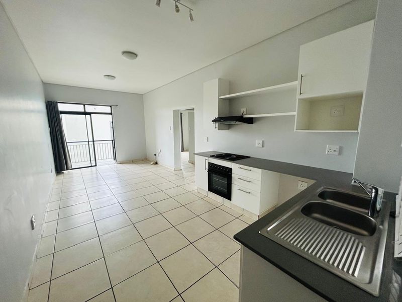 An open-plan living and kitchen area featuring tiled floors, built-in cabinetry, integrated appliances, and access to a balcony.