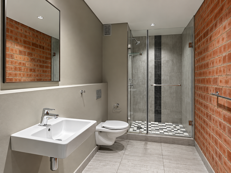 Modern bathroom featuring a wall-mounted basin, wall-hung toilet, glass-enclosed shower, and a striking exposed brick feature wall with contemporary finishes.