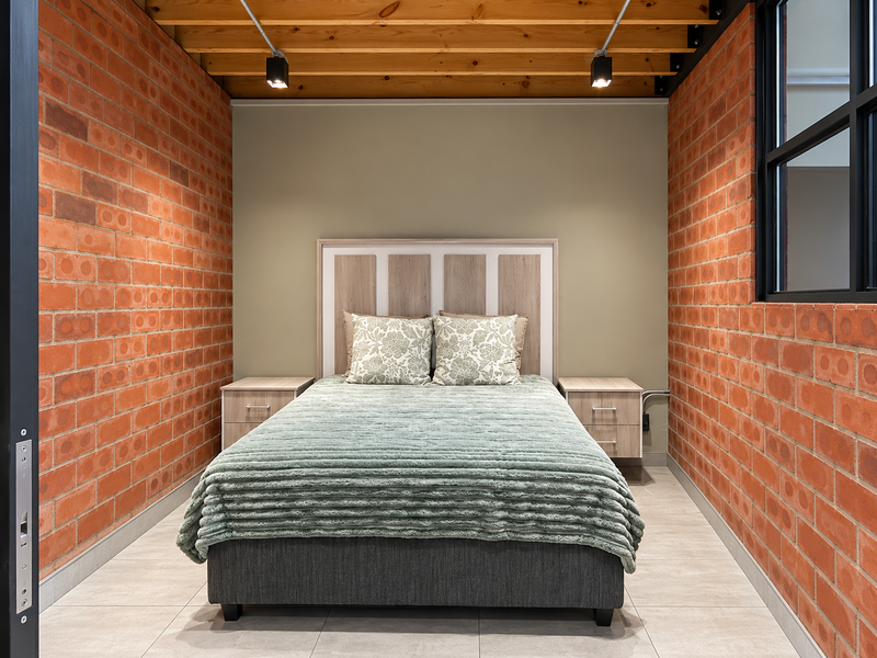 A modern bedroom featuring exposed brick walls, timber ceiling beams, and tiled flooring, creating a contemporary industrial aesthetic.