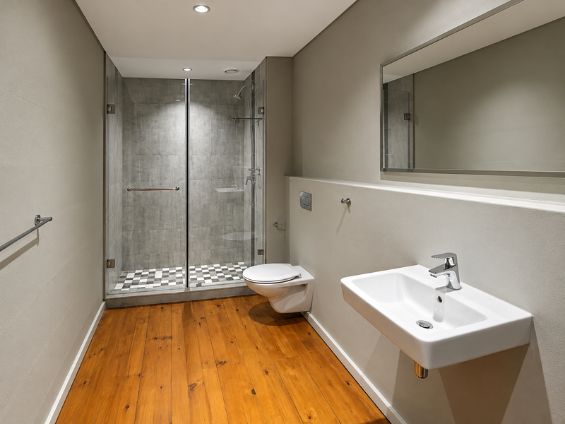 Modern bathroom featuring a wall-mounted basin, wall-hung toilet, and a glass-enclosed shower with tiled finishes and warm timber flooring.