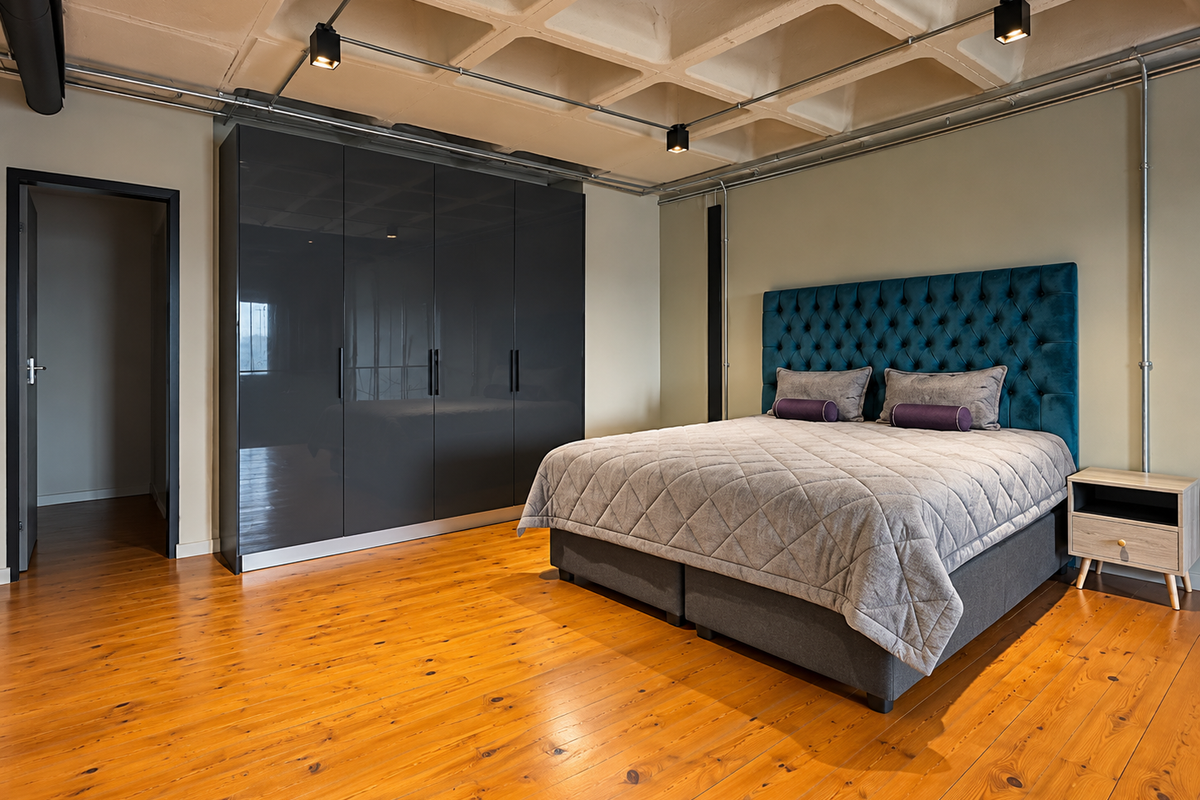 Modern bedroom featuring a unique coffered concrete ceiling, exposed industrial-style lighting, polished hardwood floors, and a sleek built-in high-gloss wardrobe.