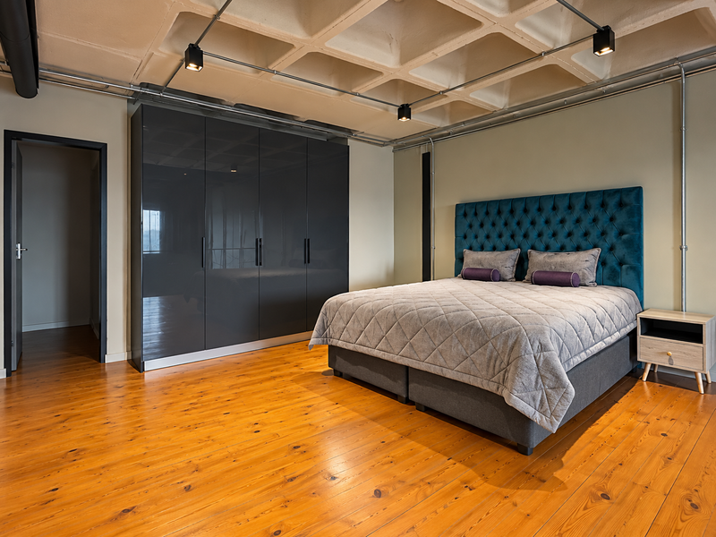 Modern bedroom featuring a unique coffered concrete ceiling, exposed industrial-style lighting, polished hardwood floors, and a sleek built-in high-gloss wardrobe.