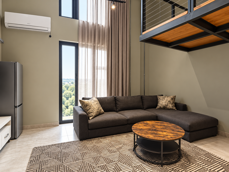 Modern double-volume living area featuring high ceilings, large windows with natural light, and a mezzanine level with industrial-style steel detailing.