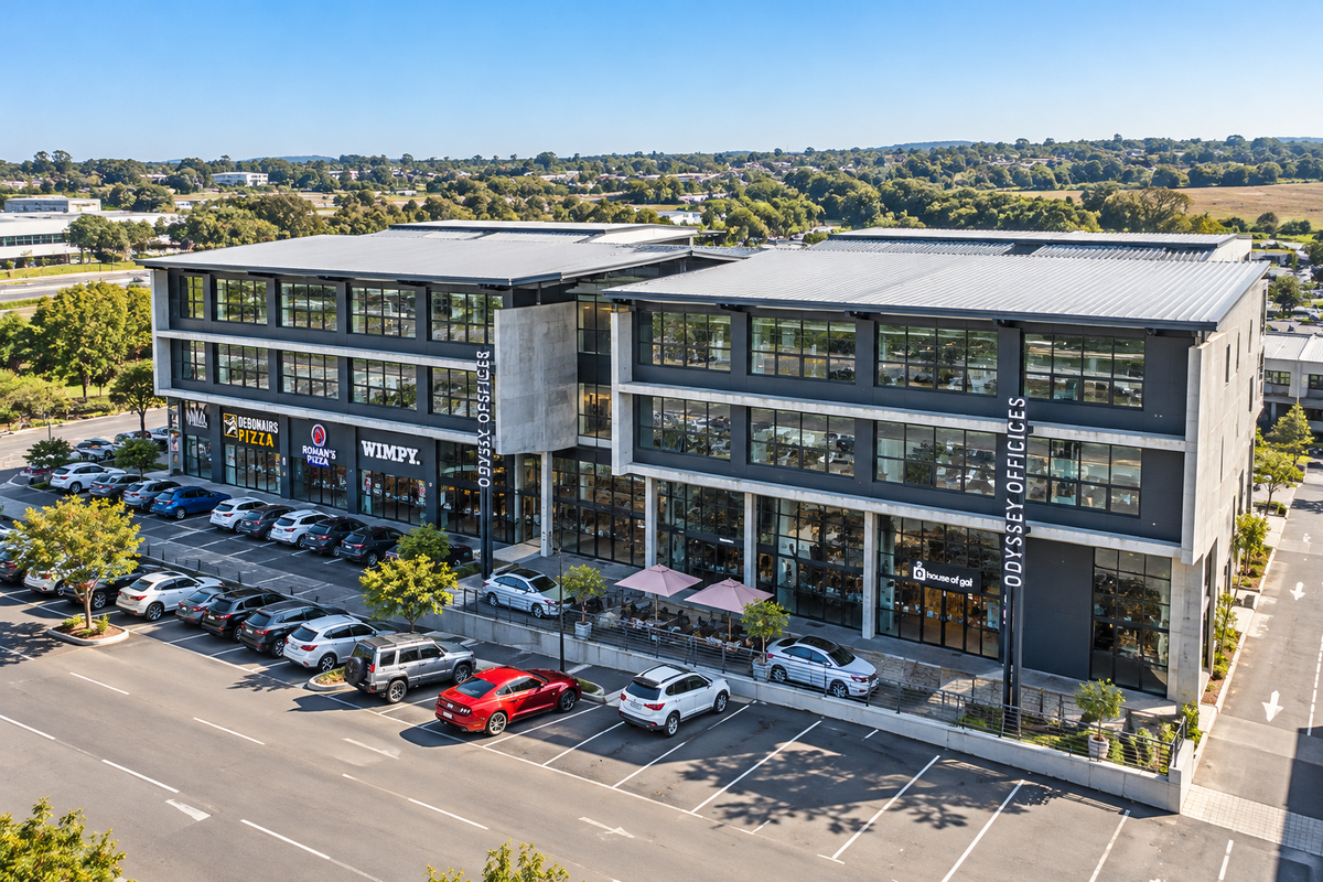 Aerial view of a modern multi-story commercial building featuring ground-floor retail spaces, office levels, and an adjacent paved parking area.