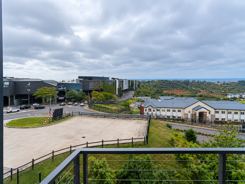 Elevated view overlooking the surrounding estate, paved parking area, and distant coastal landscape from a balcony.