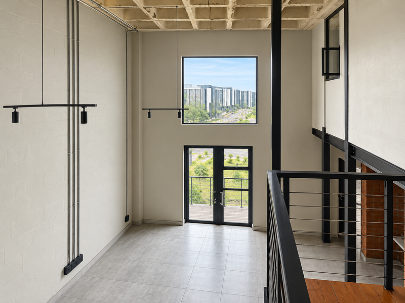 Spacious double-volume living area featuring industrial-style exposed concrete ceilings, steel structural elements, tiled flooring, and large windows with views.