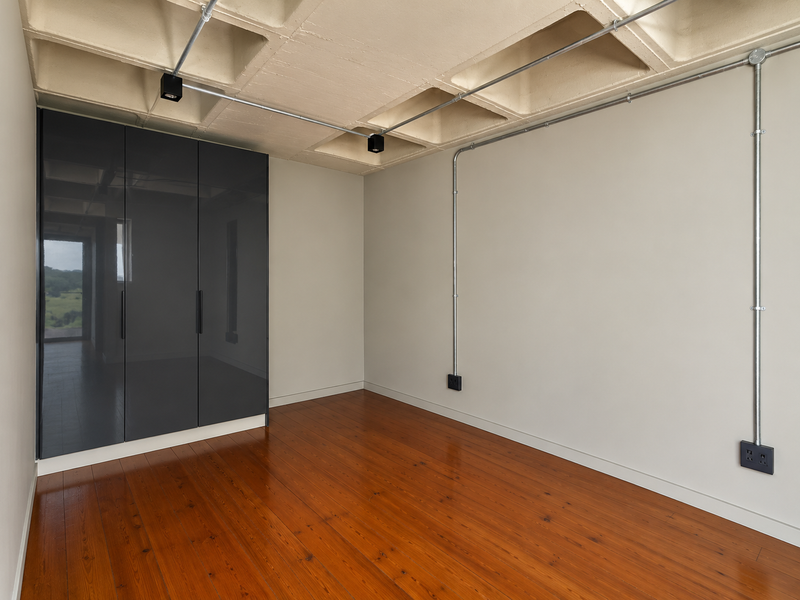 Modern bedroom featuring polished hardwood floors, built-in dark grey cabinetry, and an industrial-style exposed concrete waffle ceiling with surface-mounted electrical conduits.
