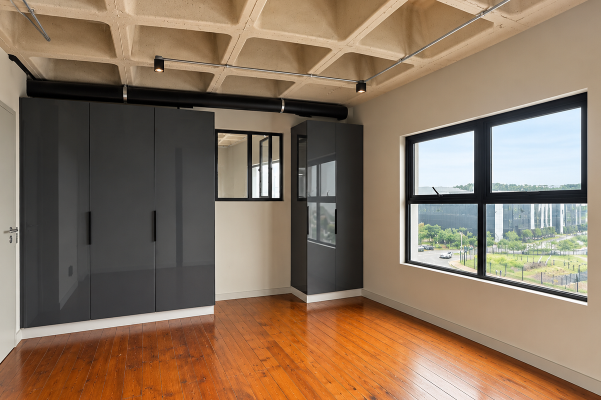A modern, empty bedroom featuring a unique exposed concrete waffle ceiling, polished hardwood floors, built-in dark grey cabinetry, and large windows with exterior views.