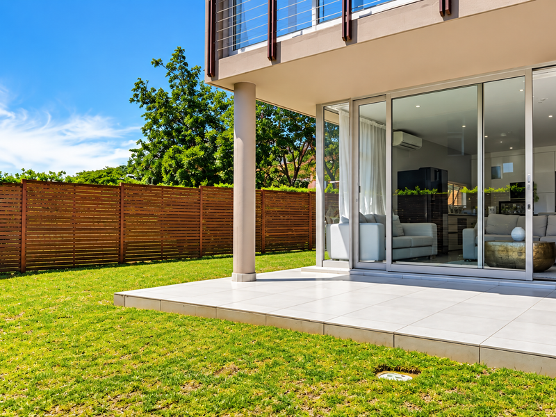 A well-maintained ground floor patio featuring large sliding glass doors, tiled flooring, and a private garden area with a wooden boundary fence.