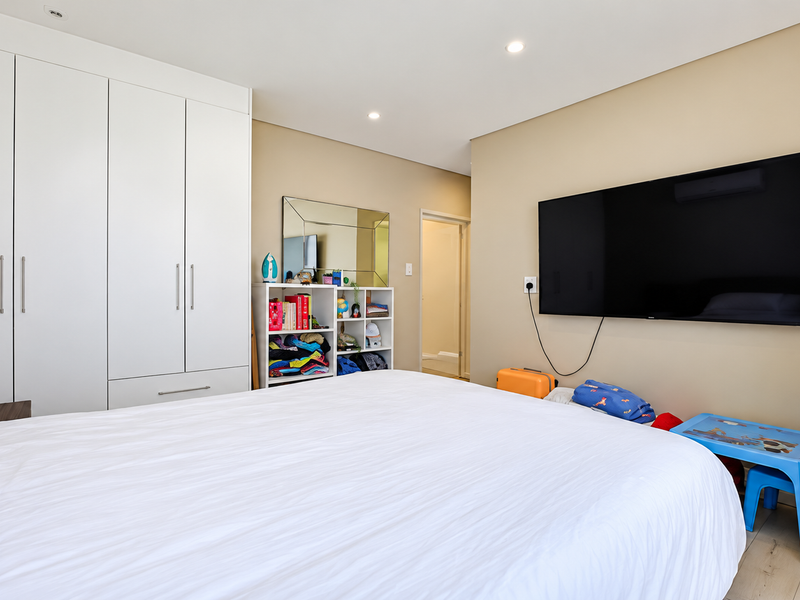 A well-maintained bedroom featuring ample built-in cupboard storage, recessed downlighting, and neutral wall finishes, providing a clean and functional living space.