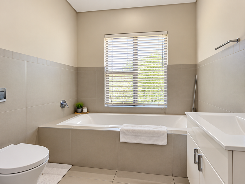 Modern bathroom featuring a built-in bathtub, wall-mounted toilet, vanity with basin, and neutral tiled finishes, offering a clean and contemporary aesthetic.