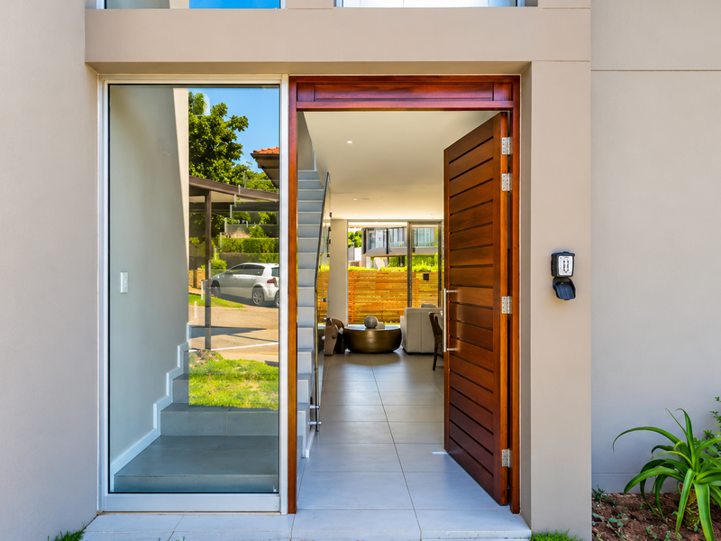 Modern apartment entrance featuring a solid timber front door, large glass sidelight, and tiled flooring leading into the open-plan living area.