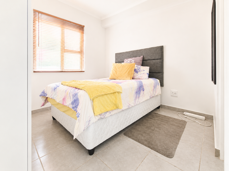 A bright and clean bedroom featuring neutral tiled flooring and natural light through venetian blinds.