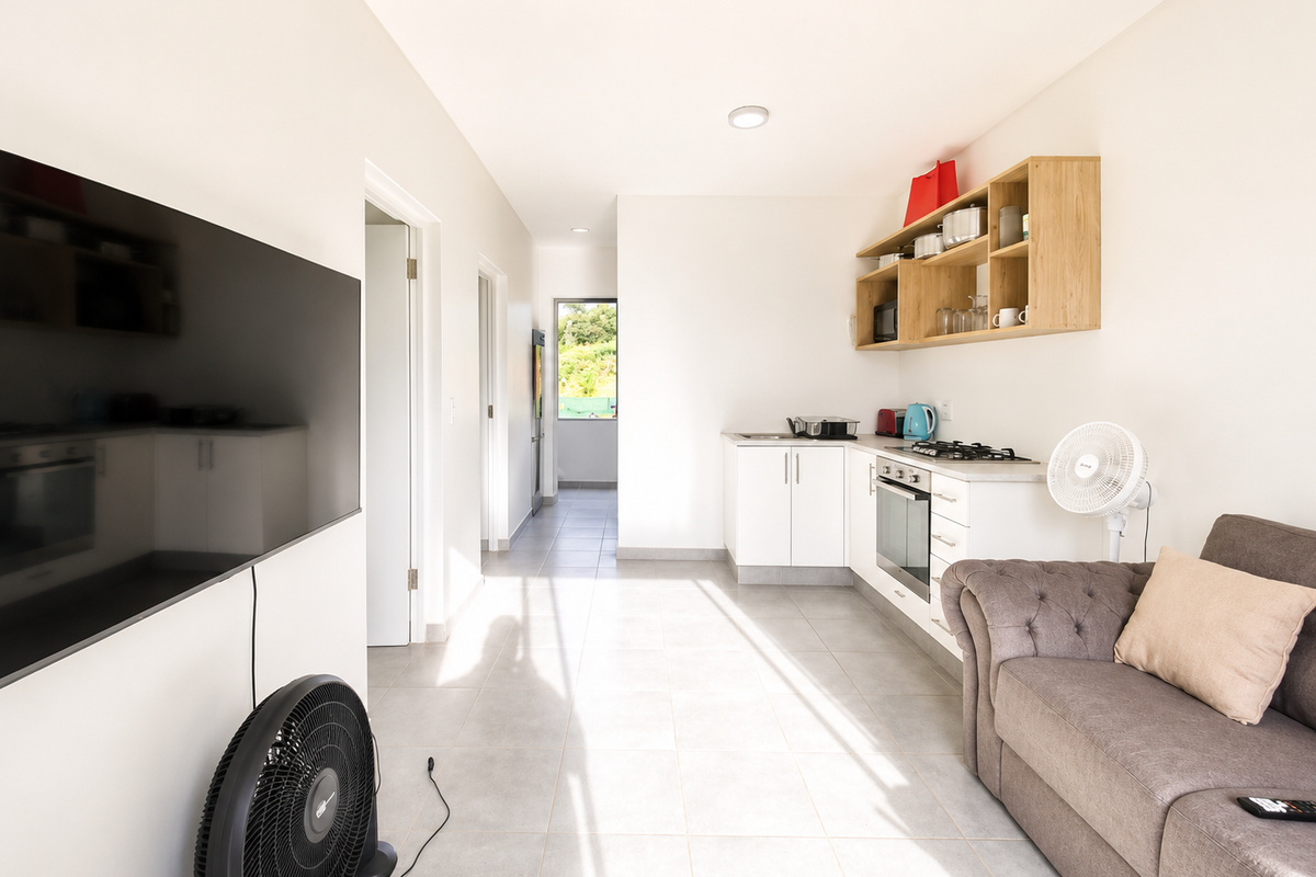 An open-plan living and kitchen area featuring tiled flooring, modern white cabinetry, built-in cooking appliances, and open wooden shelving.