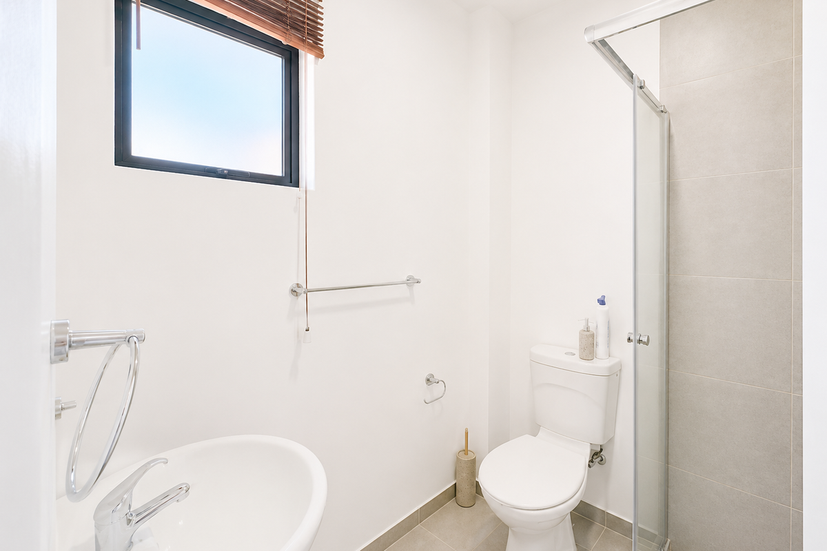 A clean and modern bathroom featuring a pedestal basin, close-coupled toilet, and a glass-enclosed shower with neutral wall and floor tiling.