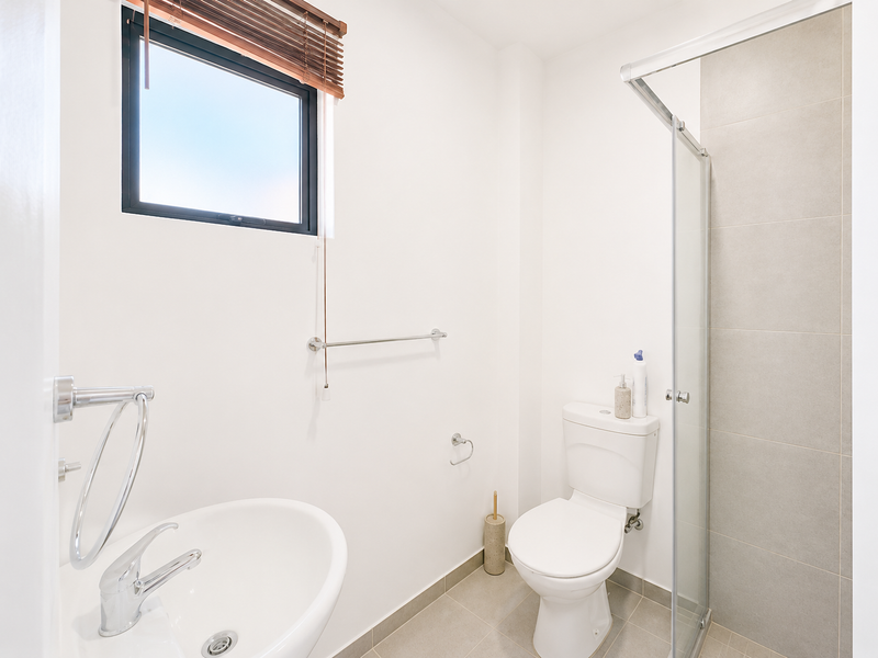 A clean and modern bathroom featuring a pedestal basin, close-coupled toilet, and a glass-enclosed shower with neutral wall and floor tiling.