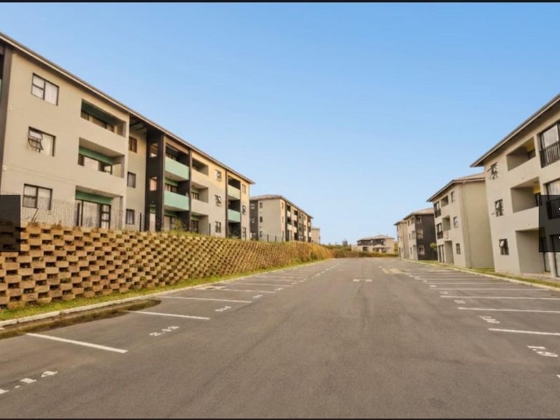 Exterior view of a modern apartment complex featuring paved parking bays and multi-story residential buildings with balconies.