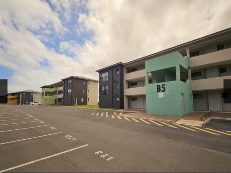 Exterior view of a modern apartment complex featuring a paved parking area and multi-story residential blocks with designated unit numbering.