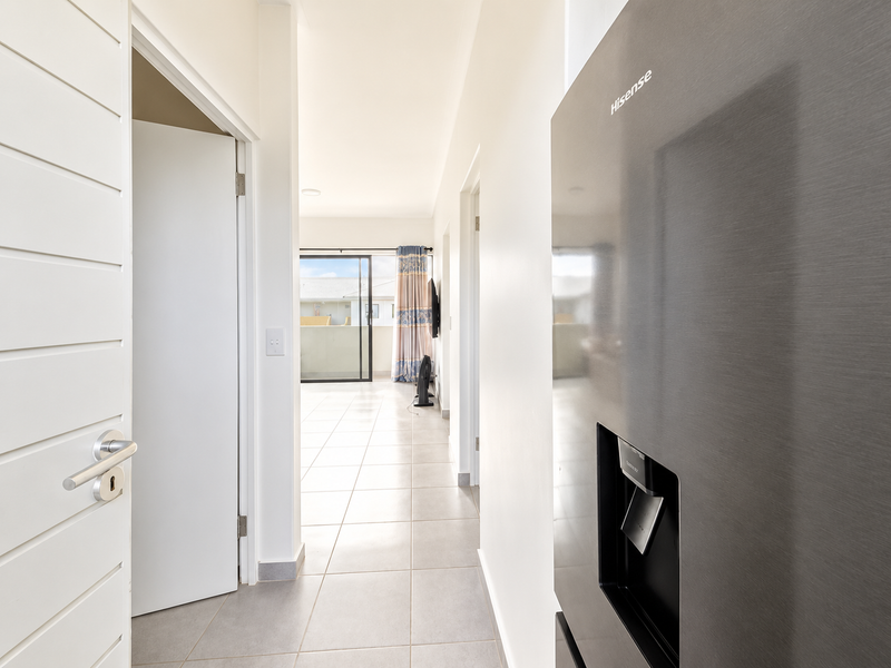 A bright, tiled hallway leading from the kitchen area towards a living space with access to a balcony through sliding glass doors.