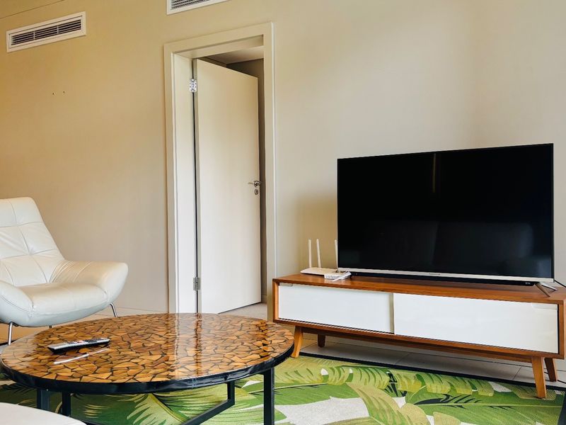 A well-lit living room featuring tiled flooring, neutral wall finishes, and integrated ducted air conditioning vents.