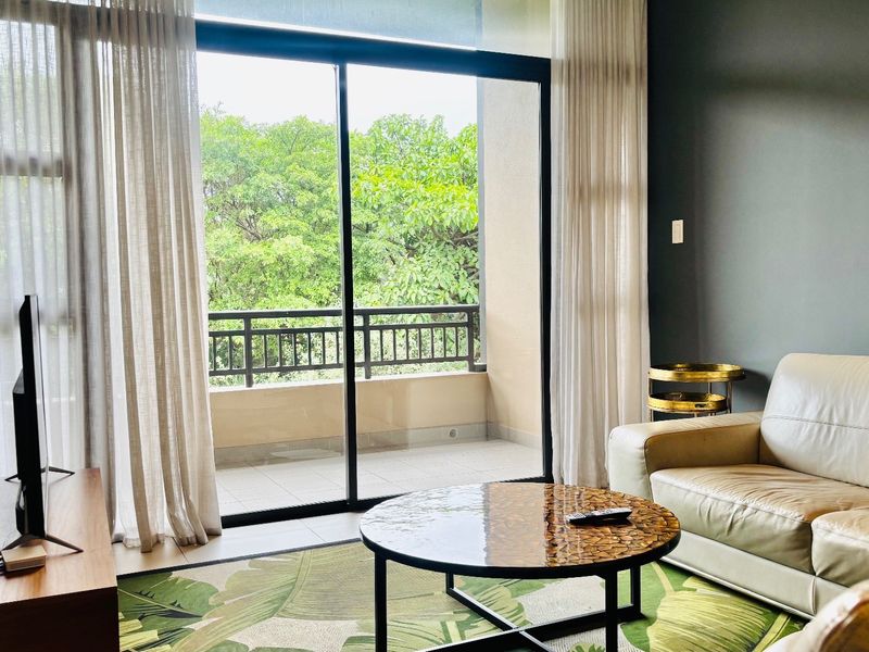 Bright living room featuring large sliding glass doors that open onto a private balcony with lush green views.