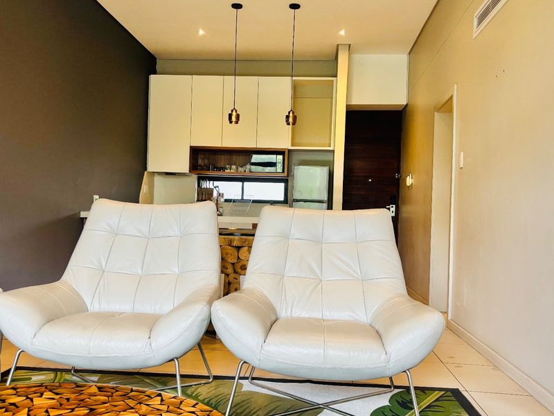 Modern open-plan living area featuring tiled floors, recessed and pendant lighting, and a compact kitchen with built-in cabinetry.