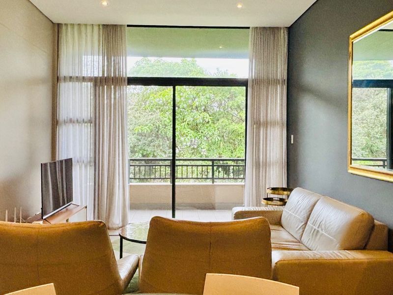 A bright and modern living room featuring large sliding glass doors that open onto a balcony with lush green views.
