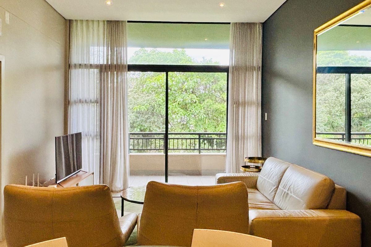 A bright and modern living room featuring large sliding glass doors that open onto a balcony with lush green views.