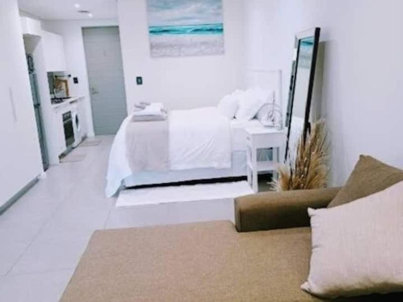 An open-plan studio apartment featuring a compact kitchen area with built-in appliances, tiled flooring, and recessed lighting throughout the living and sleeping space.