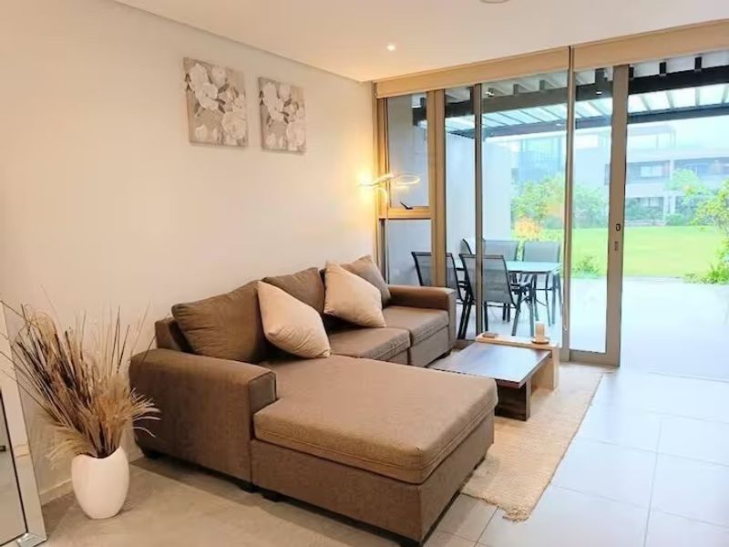 A bright living room featuring large sliding glass doors that open onto a patio, with neutral tiled flooring and modern recessed lighting.