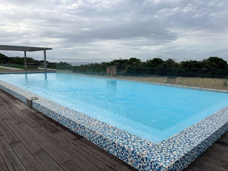 A well-maintained outdoor swimming pool area featuring modern glass balustrades, timber decking, and a pergola, offering scenic views.
