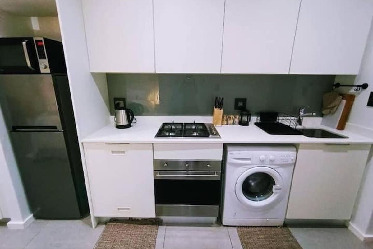 Compact modern kitchen featuring white cabinetry, stone countertops, a gas hob, built-in oven, and an integrated washing machine.