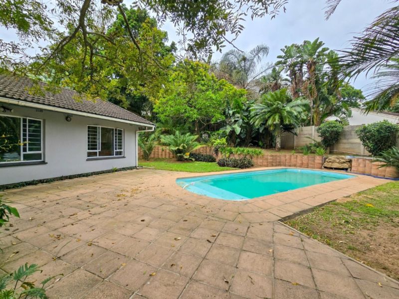A private backyard featuring a swimming pool, paved patio area, and established garden surroundings with a rear view of the house.
