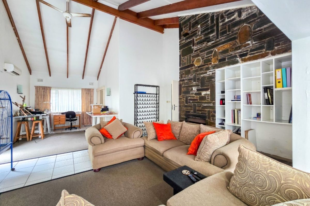 Spacious living room featuring a striking stone fireplace, exposed timber beams, and built-in shelving, offering a warm and character-filled atmosphere.