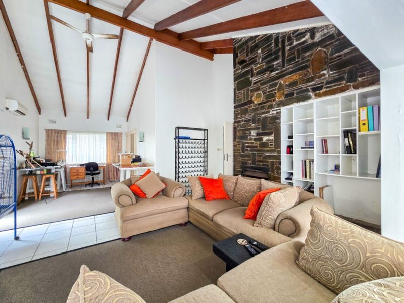 Spacious living room featuring a striking stone fireplace, exposed timber beams, and built-in shelving, offering a warm and character-filled atmosphere.