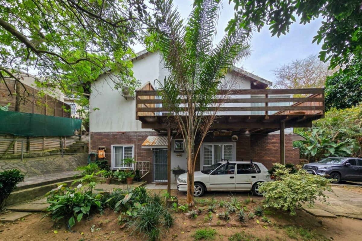 Rear view of the house featuring a raised wooden deck, brick exterior walls, and a paved ground level area with garden landscaping.