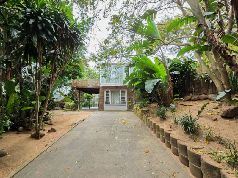 Front view of a brick house featuring a concrete driveway, a raised wooden deck, and established garden landscaping.