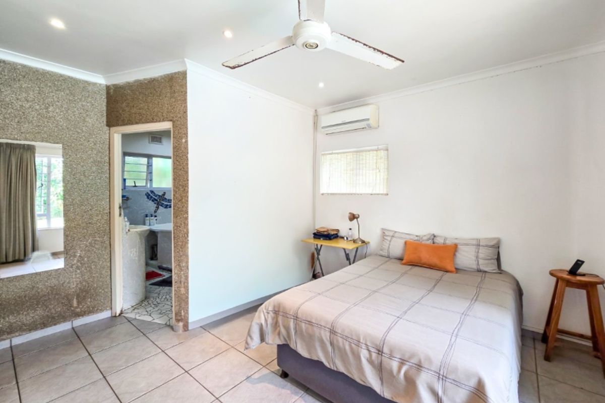 A bedroom featuring tiled flooring, a ceiling fan, and a split-system air conditioner, with an adjoining bathroom visible through the doorway.
